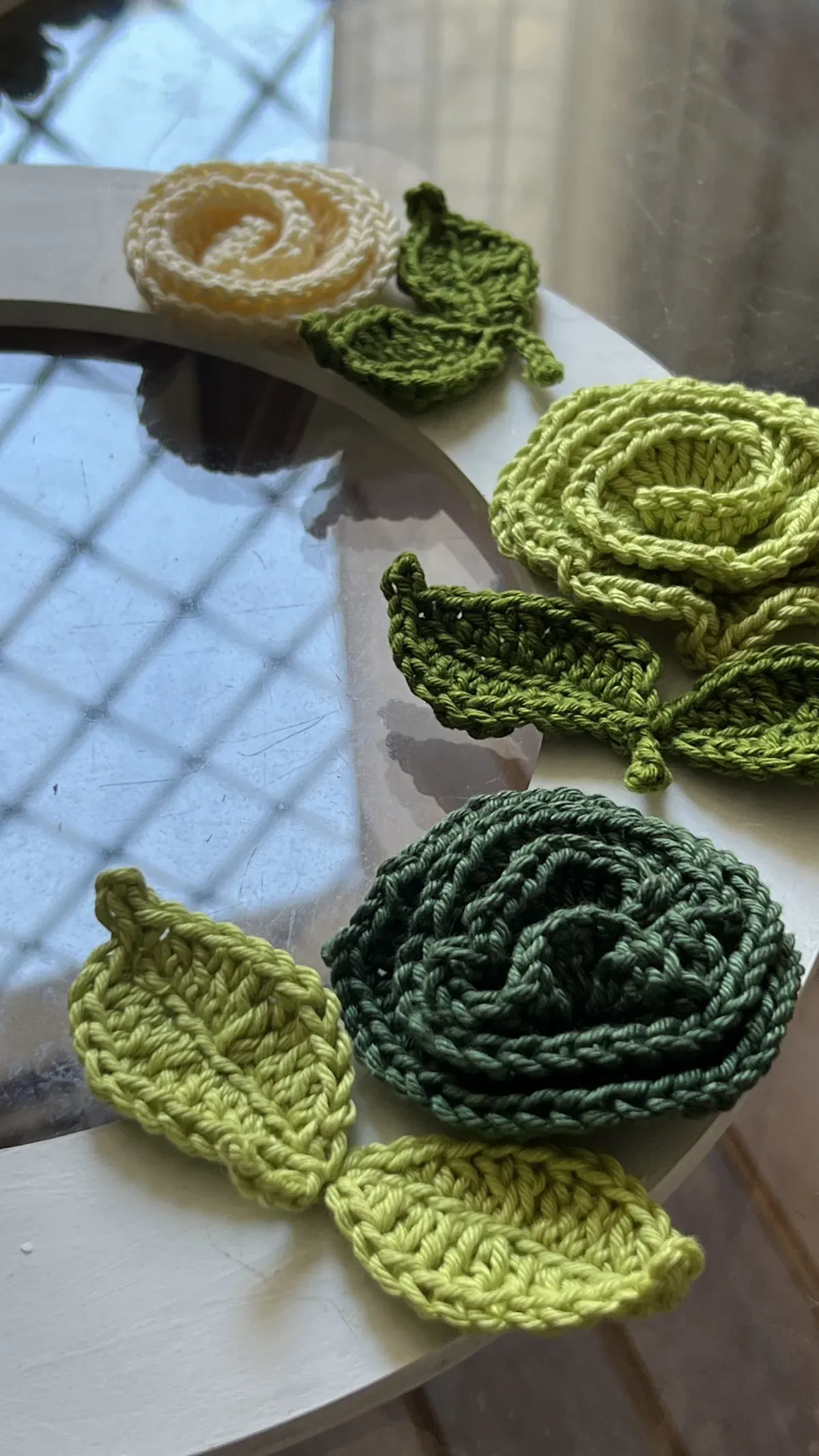 Detalhe da Flor Alice em crochê na cor creme com folhas verdes