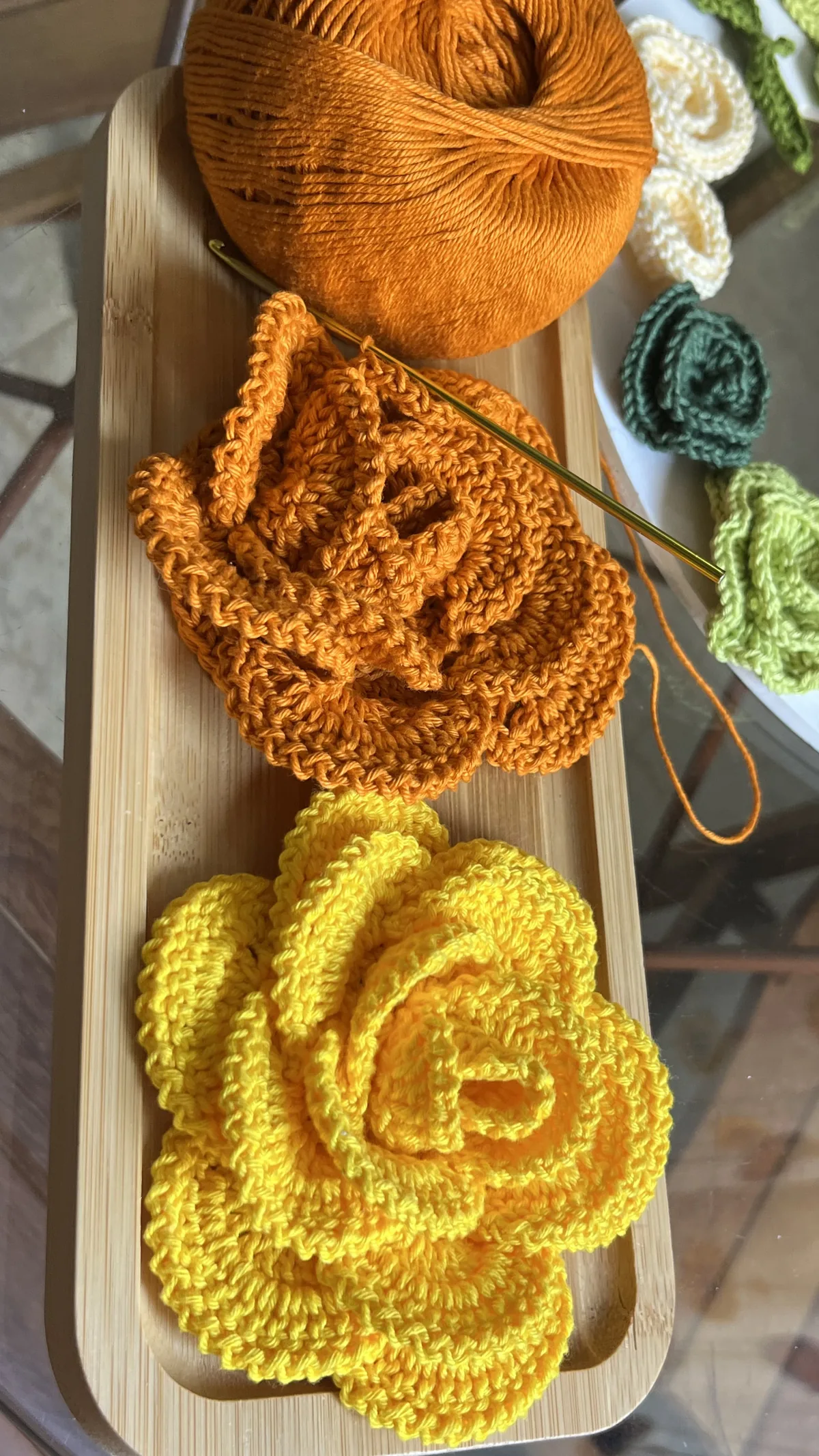 Detalhe da Flor Regina em crochê laranja sendo confeccionada com agulha