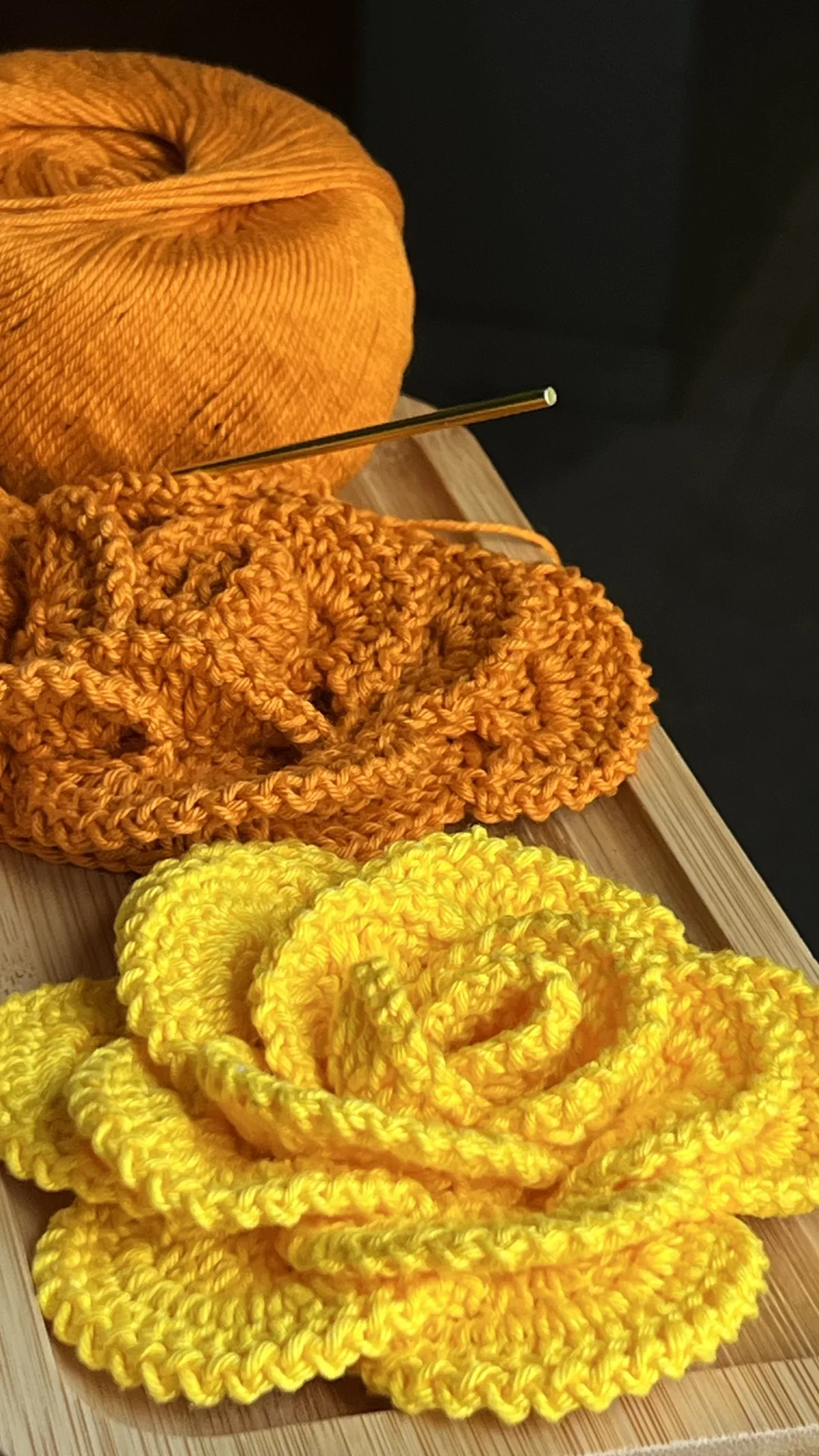 Novelo de linha laranja com agulha de crochê ao lado das Flores Regina prontas