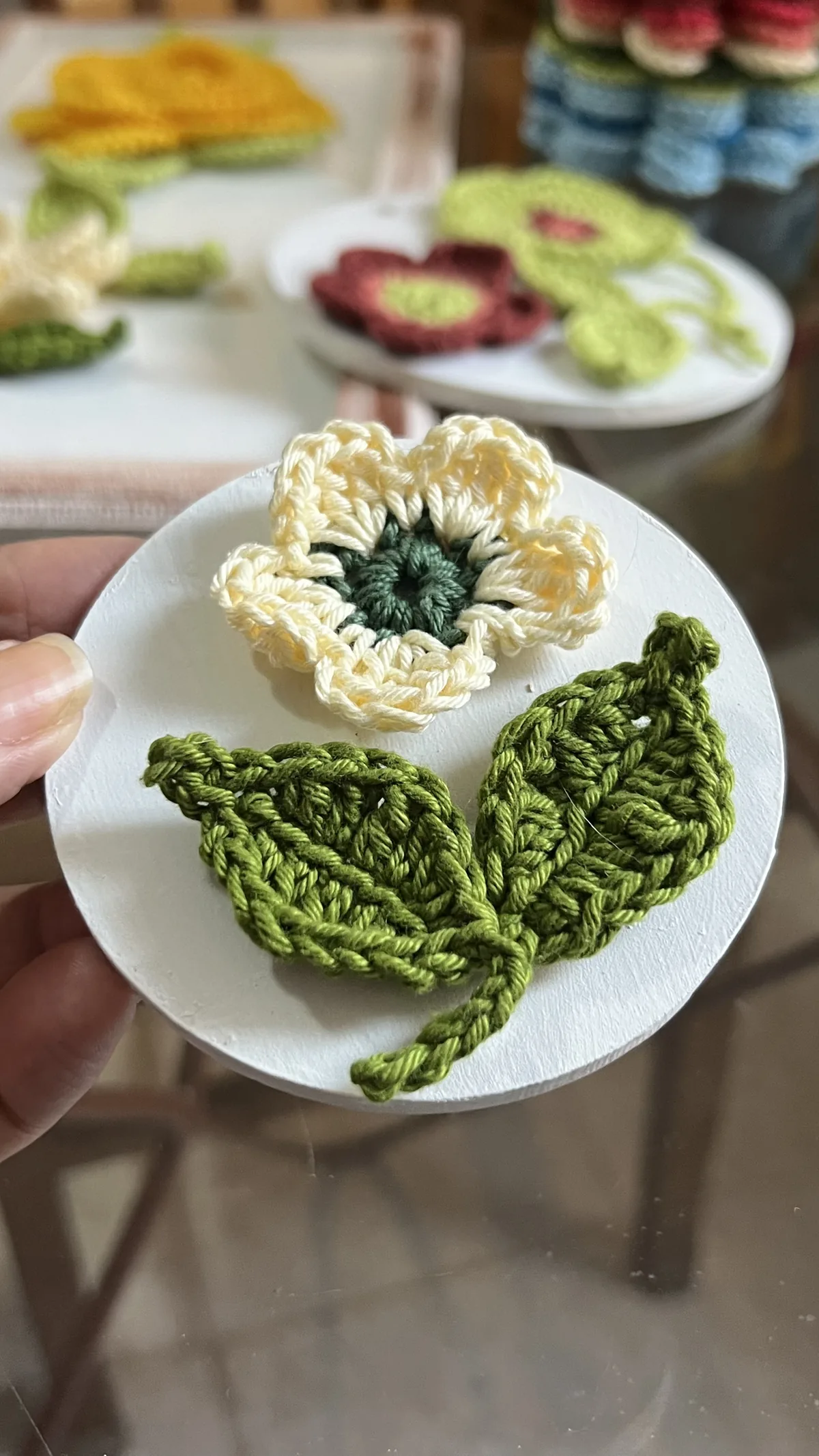 Flor creme de crochê com duas folhas em base decorativa